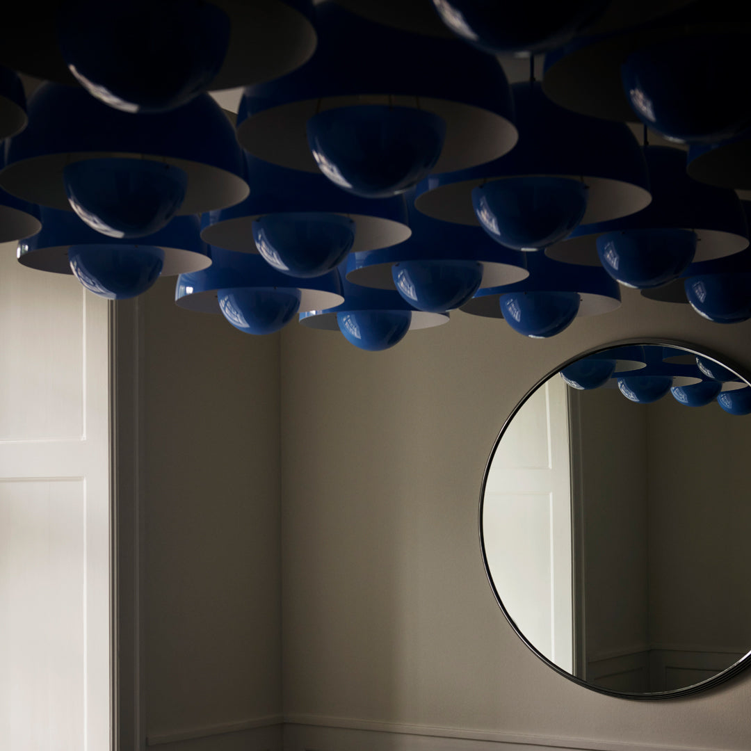 Blue and white ceiling light fixtures create a modern pattern, reflecting elegantly in a circular mirror.