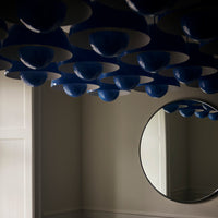 Blue and white ceiling light fixtures create a modern pattern, reflecting elegantly in a circular mirror.