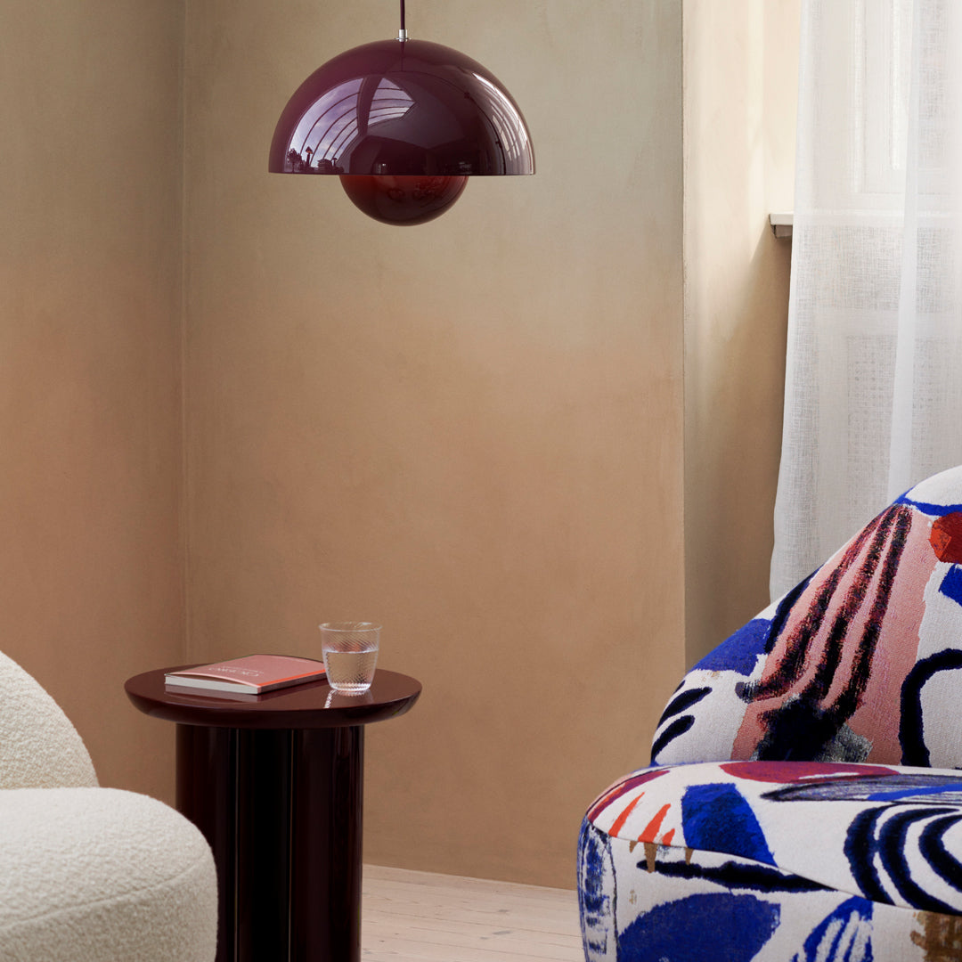 "Deep burgundy pendant lamp above a colorful, abstract-patterned chair in a soft beige room."