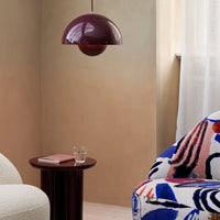 Round burgundy pendant lamp above a decorative table next to a vibrant, patterned chair in blue, red, and white hues.