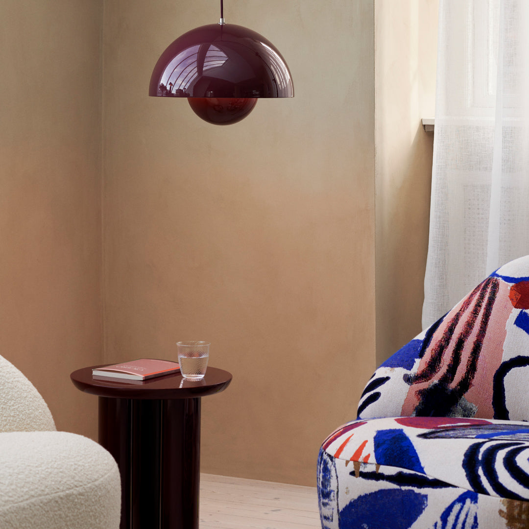 Colorful patterned chair featuring bold blues, reds, and abstract shapes, with a sleek burgundy pendant lamp above.