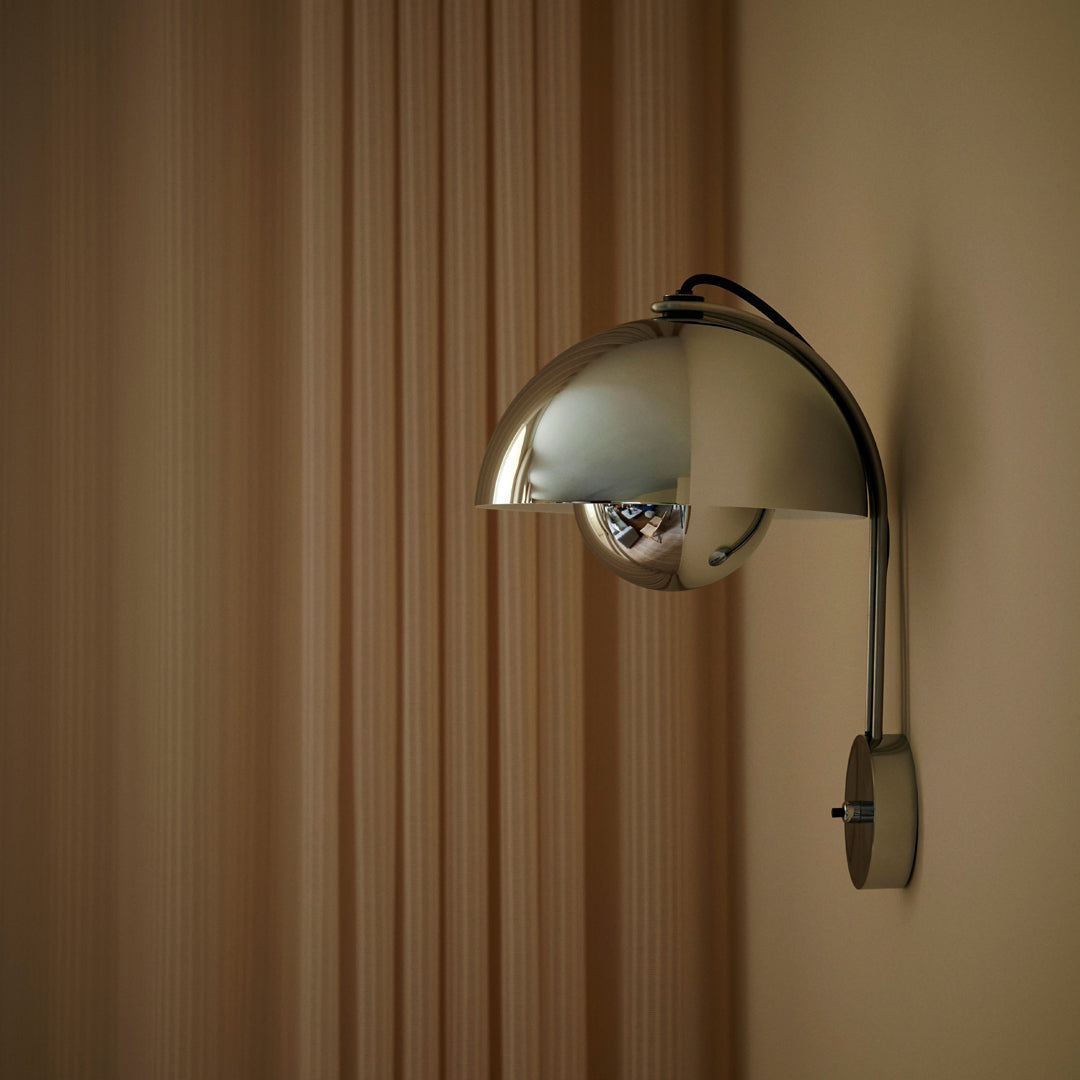 Sleek chrome wall lamp with a round shade, set against a warm beige wall and vertical striped backdrop.