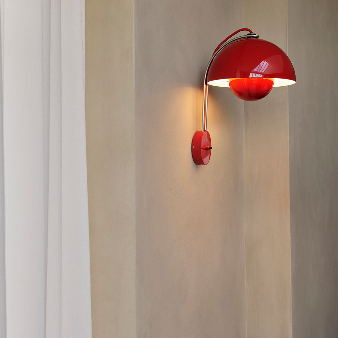 Red curved wall lamp with a glossy finish, casting warm light on a beige wall texture. Stylish and modern decor accent.