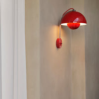 Red curved wall lamp with a glossy finish, casting warm light on a beige wall texture. Stylish and modern decor accent.