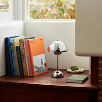 "Modern chrome lamp beside colorful books in blue, orange, and yellow on a wooden tabletop."