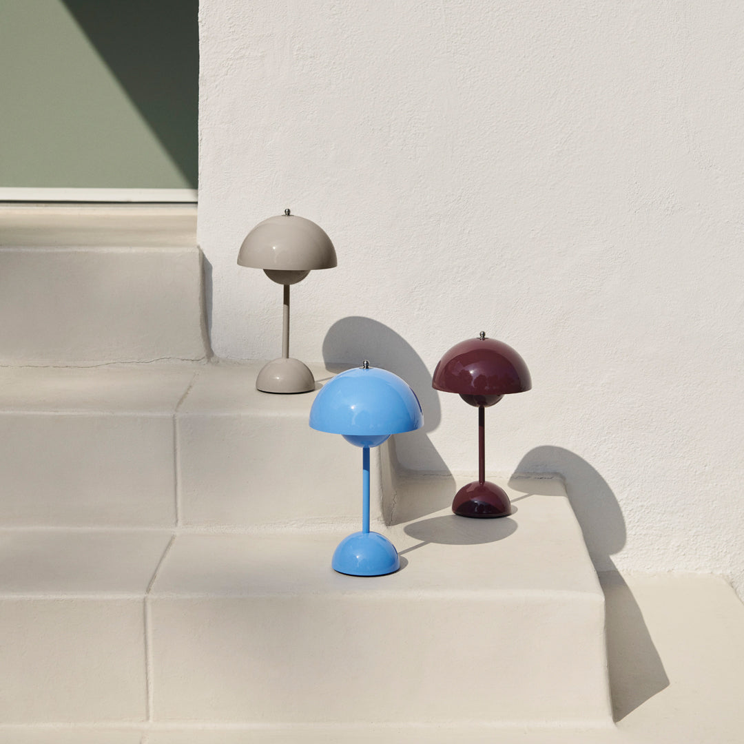 Three modern lamp designs in beige, blue, and burgundy on light-colored steps against a minimalistic background.