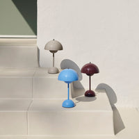 Three modern lamp designs in beige, blue, and burgundy on light-colored steps against a minimalistic background.