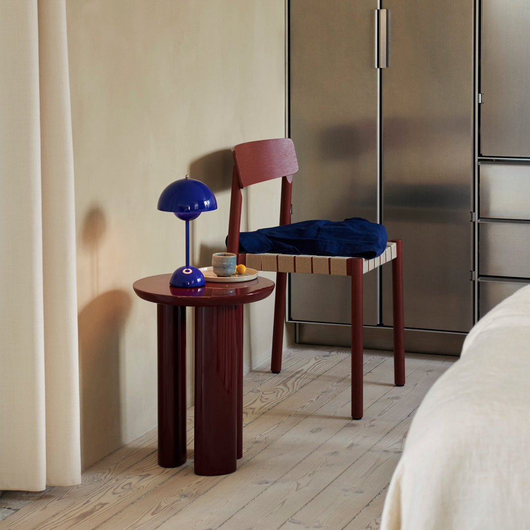 Red and blue chair and lamp with a round red table, set against a neutral wall and light wood floor.