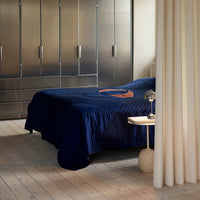 Navy blue bedspread with striped pattern and copper detailing in a modern bedroom setting.