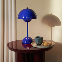 Modern blue table lamp on a round burgundy table, complemented by a textured teal cup and neutral-colored fruits.