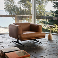 Brown leather armchair with minimalist design, resting on a sleek black base against a natural stone floor.
