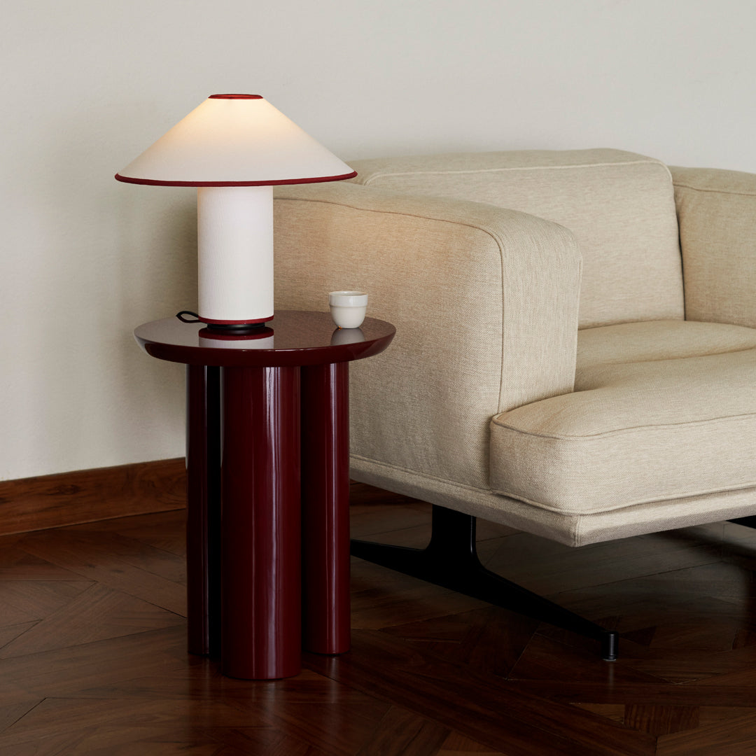 Modern table lamp featuring a white shade, red accents, and a smooth, cylindrical burgundy base against a neutral background.