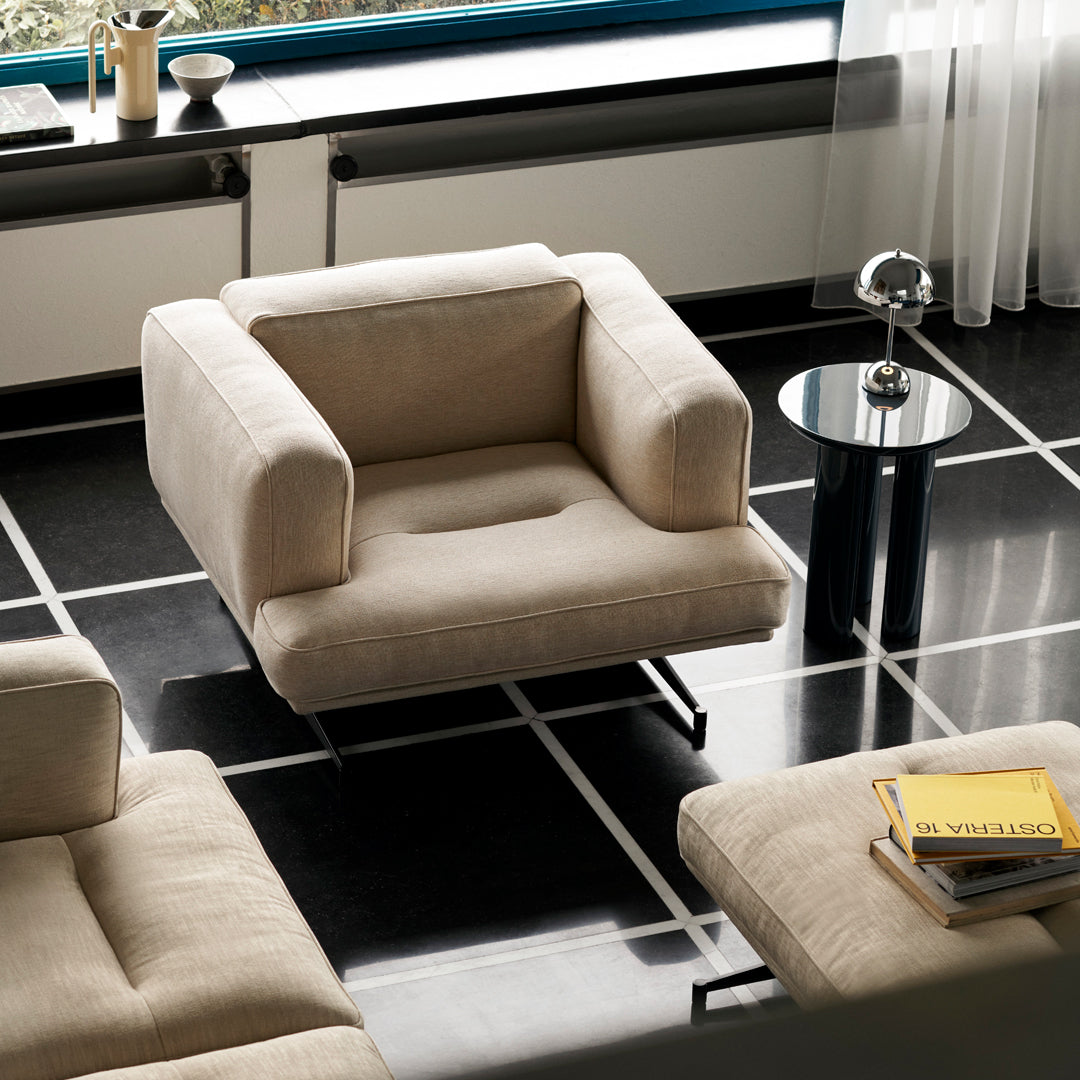 Beige upholstered armchair on black and white tiled floor. Modern design with clean lines and minimalist elegance.