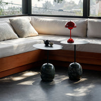 "Modern side tables with smooth black tops and sculptural green bases, complemented by a vibrant red lamp."