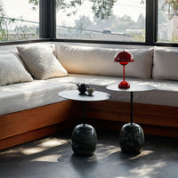 Modern living room with white cushions, round black tables, and a bright red lamp, featuring sleek patterns and textures.