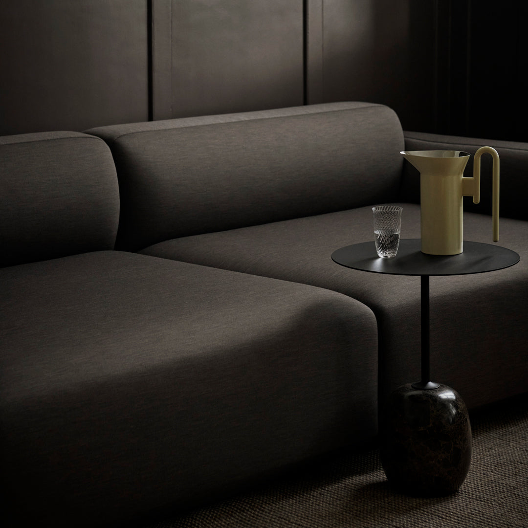 Dark charcoal sofa with smooth upholstery, paired with a minimalist black side table and soft yellow pitcher.