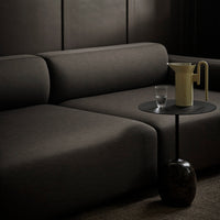 Dark charcoal sofa with smooth upholstery, paired with a minimalist black side table and soft yellow pitcher.