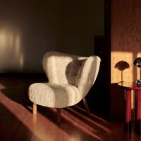 Cozy cream-colored chair with a soft, textured pattern and natural wooden legs, set against warm lighting.