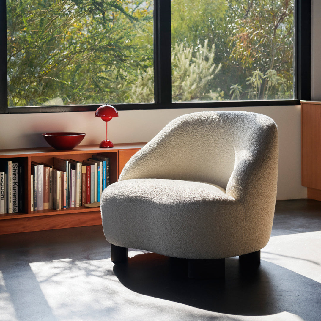 Cozy cream-colored curved chair with a textured finish, set against a backdrop of natural greenery and warm wood tones.