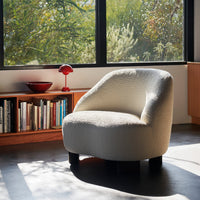 Cream-colored, curved accent chair with textured fabric, featuring black legs against a modern interior backdrop.
