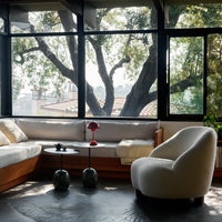Neutral beige sofa and curved white armchair, accented with bold red and green decorative elements, against a natural backdrop.
