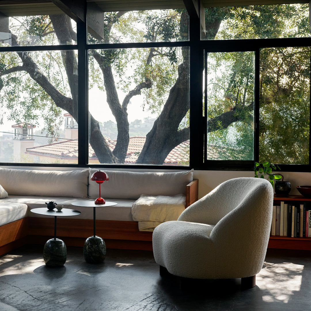 Cozy living room featuring soft white fabric chair, earthy tones, and natural light highlighting greenery outside.
