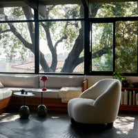 Cozy living room featuring soft white fabric chair, earthy tones, and natural light highlighting greenery outside.