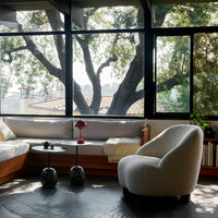 Cozy living room featuring neutral upholstery, a dark coffee table, and vibrant red lamp against a backdrop of greenery.