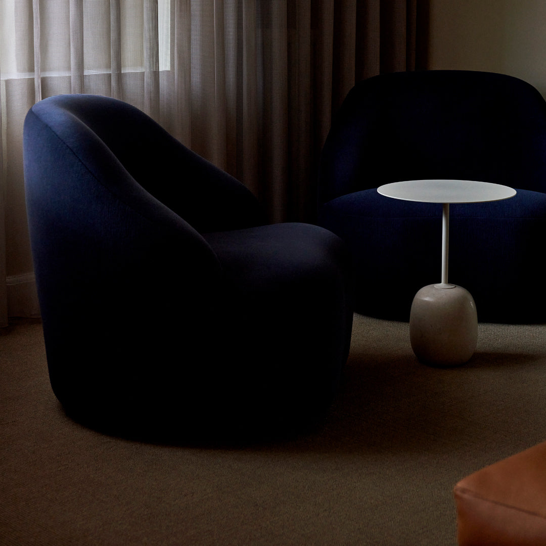 Navy blue curved chairs with a sleek white table against warm beige carpet and soft natural light.