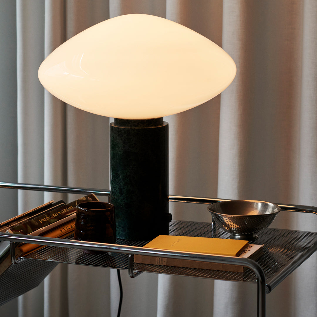 Ovoid white glass lamp on a dark green base, paired with metallic and golden accents in a modern setting.