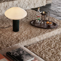 Modern white mushroom lamp on a textured green base, set against a neutral-toned stone backdrop.