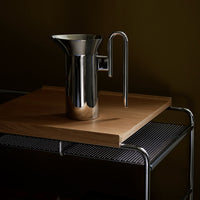 Stainless steel pitcher with a sleek, reflective surface on a wooden tabletop, complemented by a modern metal stand.