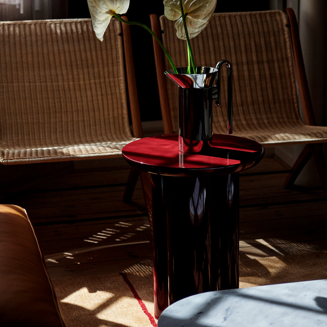 Modern black and red glossy side table, complemented by soft textures from natural wicker chairs in a stylish setting.