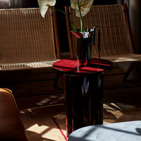 Modern black and red glossy side table, complemented by soft textures from natural wicker chairs in a stylish setting.