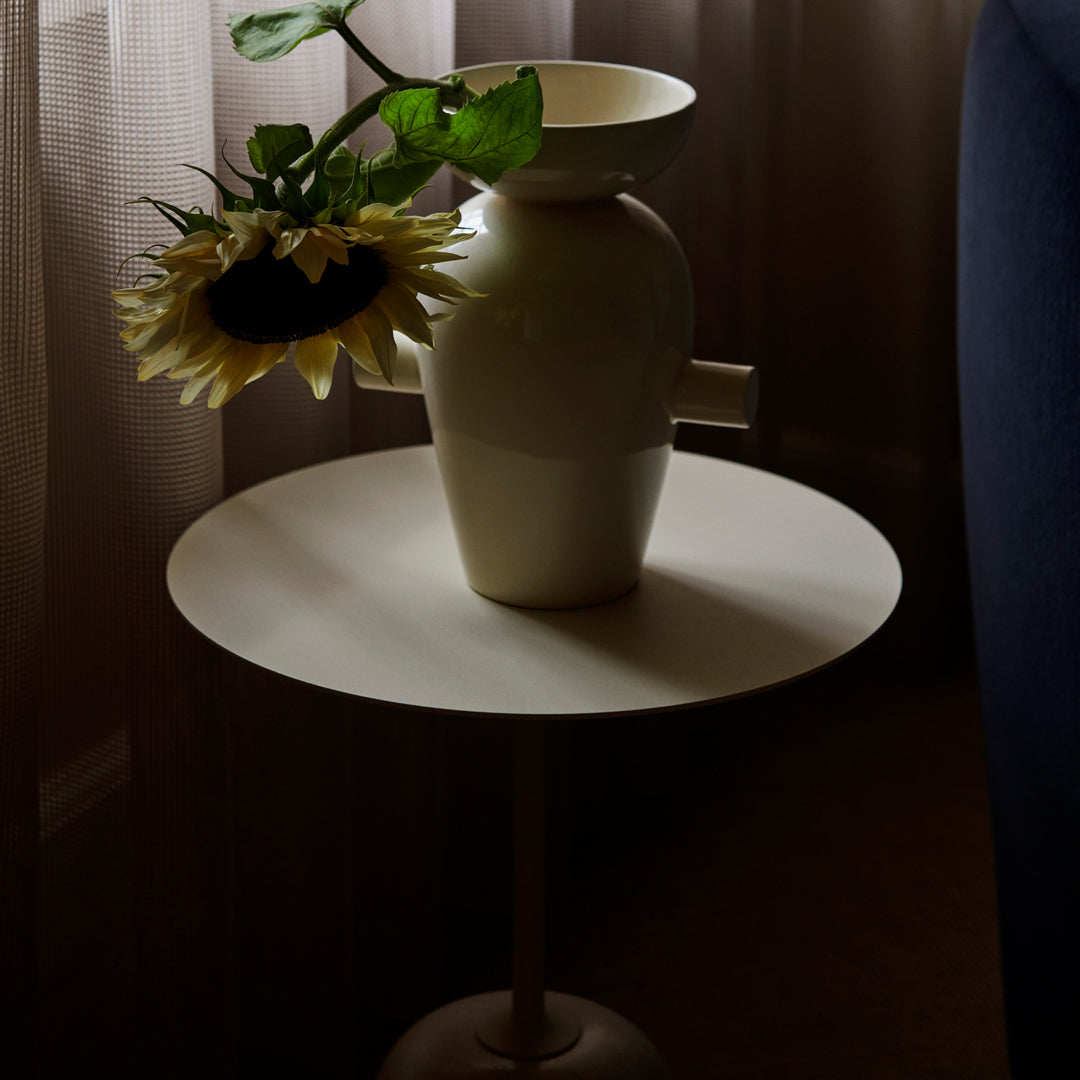 Cream vase on a minimalist white table, with a sunflower adding a pop of yellow against soft, muted decor.