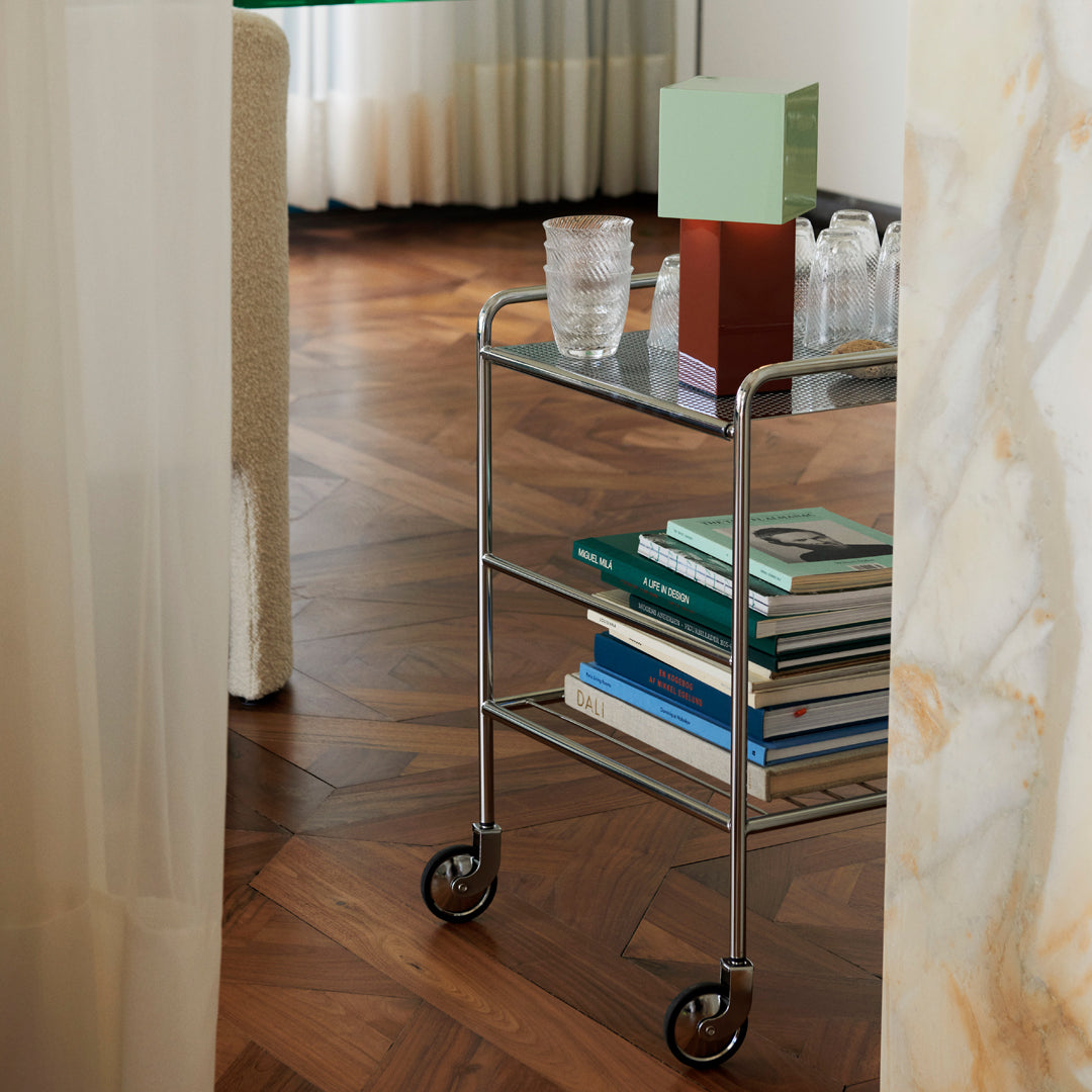 Stylish metal cart with a glass top, featuring white, green, and brown elements against a warm wood floor backdrop.