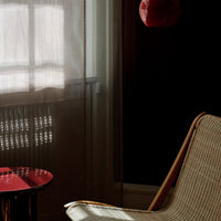 Textured beige armchair with a red circular table and sheer white curtains against a dark wall. Warm and inviting colors.