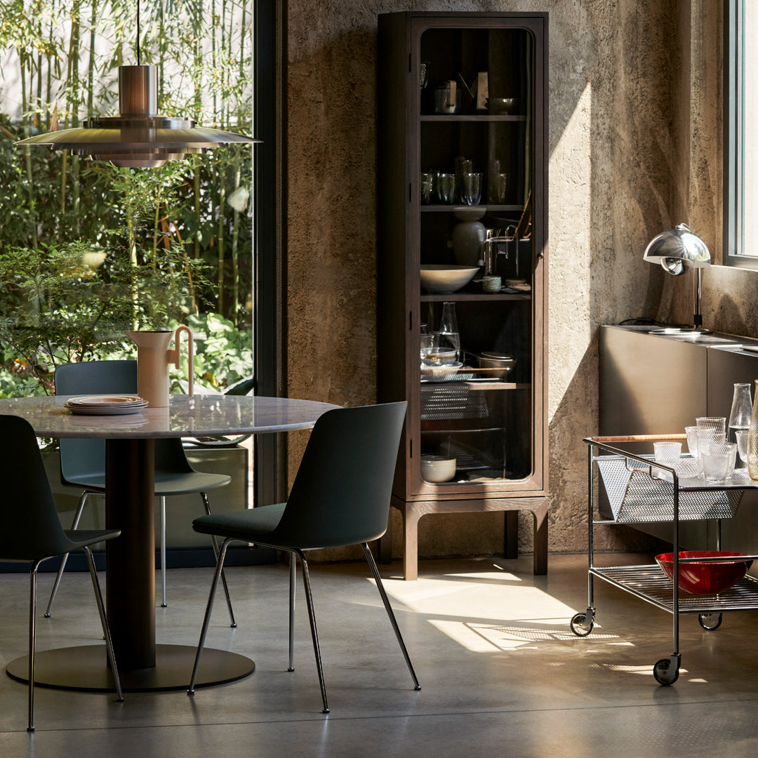 Modern dining room featuring dark green chairs, a warm wood table, and neutral-toned decor against a backdrop of greenery.