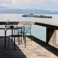 "Modern black metal chairs with geometric patterns on a stone patio overlooking a serene lake and distant island."