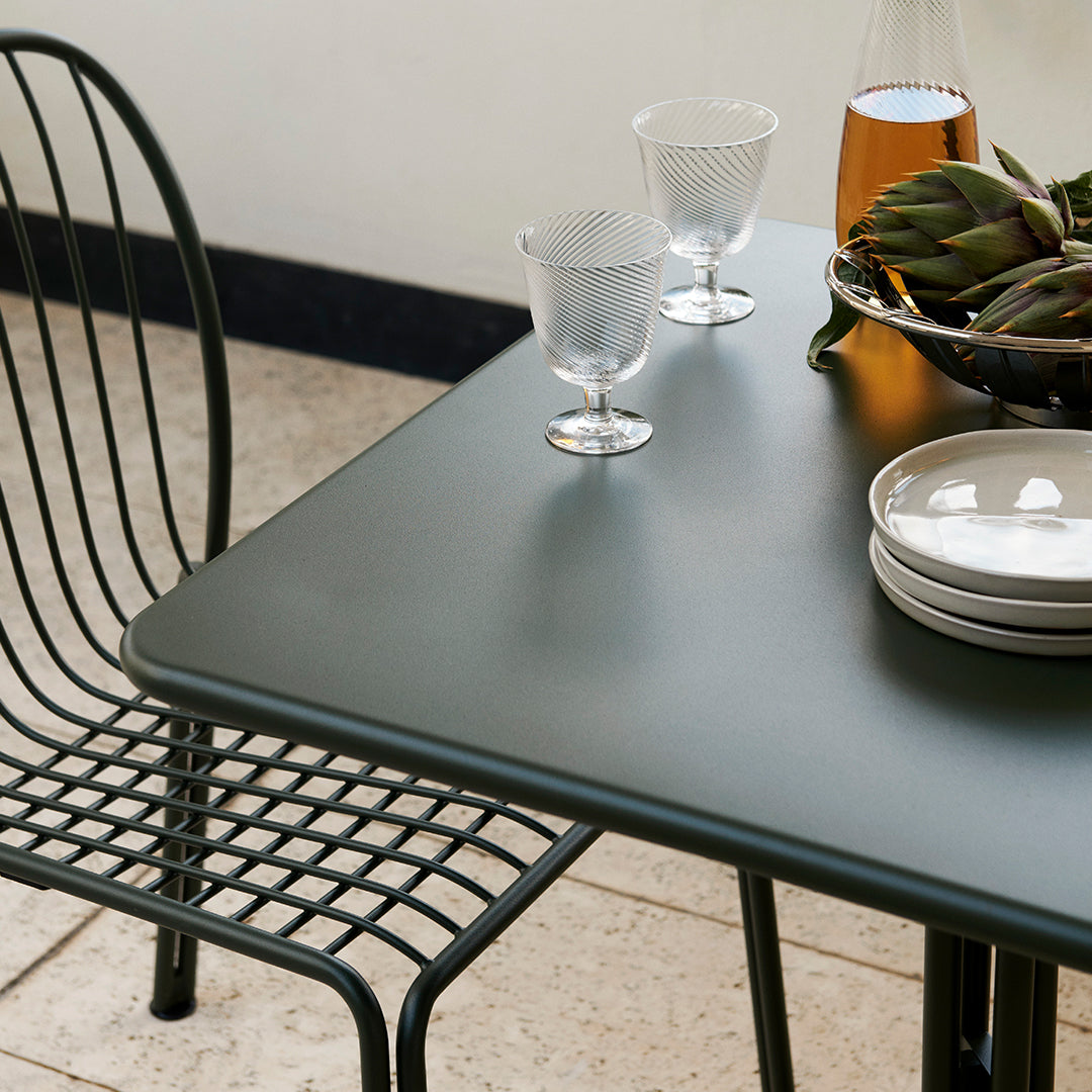 Dark green table with sleek finish, paired with black wireframe chairs and clear glassware for a modern aesthetic.