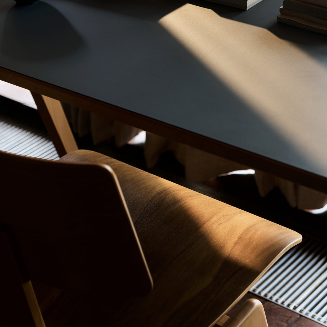 Wooden chair with a warm, natural finish beside a sleek gray table under soft morning light, highlighting shadows.