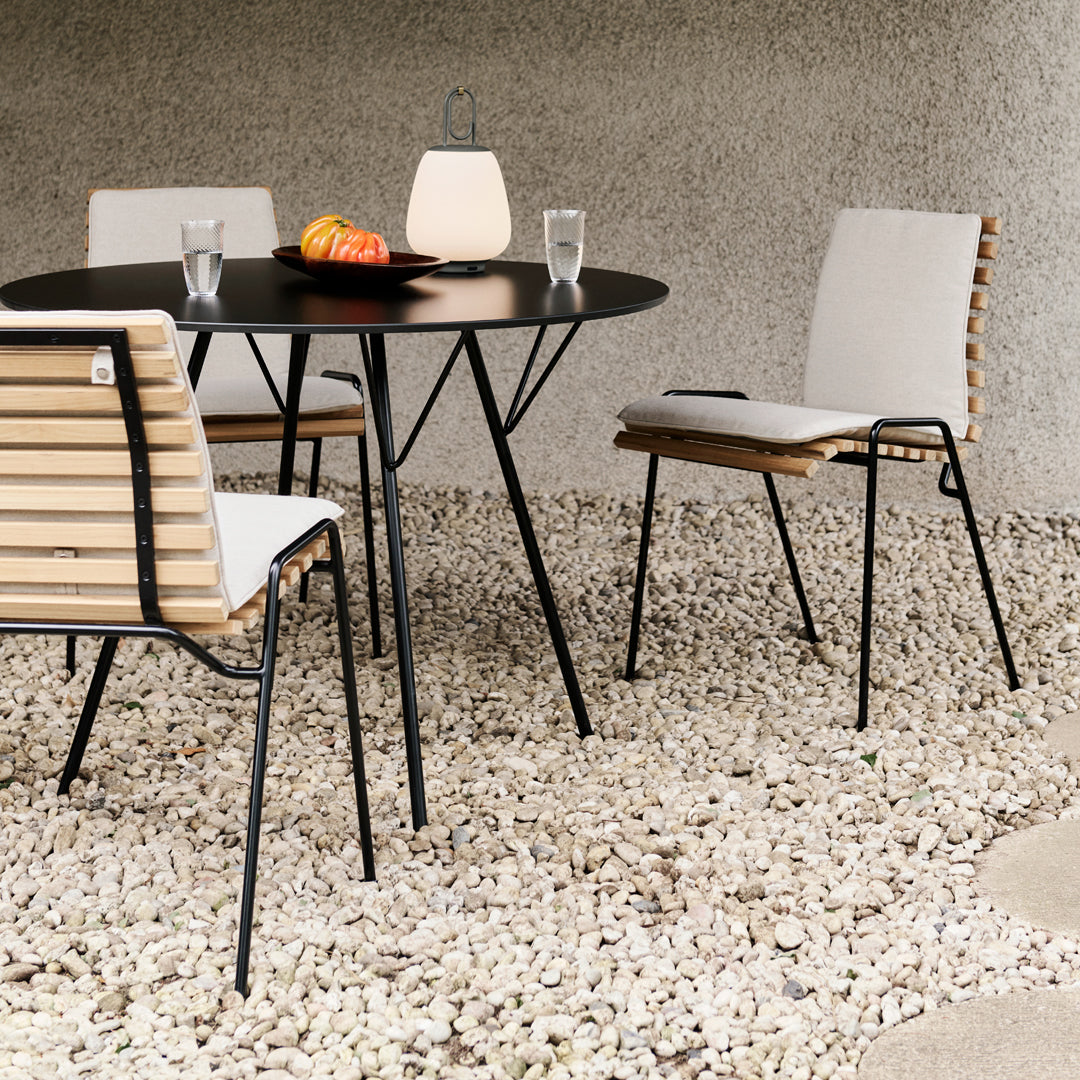 Modern outdoor dining set featuring black metal frame, natural wood accents, and white cushions on stylish striped chairs.