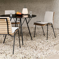 Modern outdoor dining set featuring black metal frame, natural wood accents, and white cushions on stylish striped chairs.