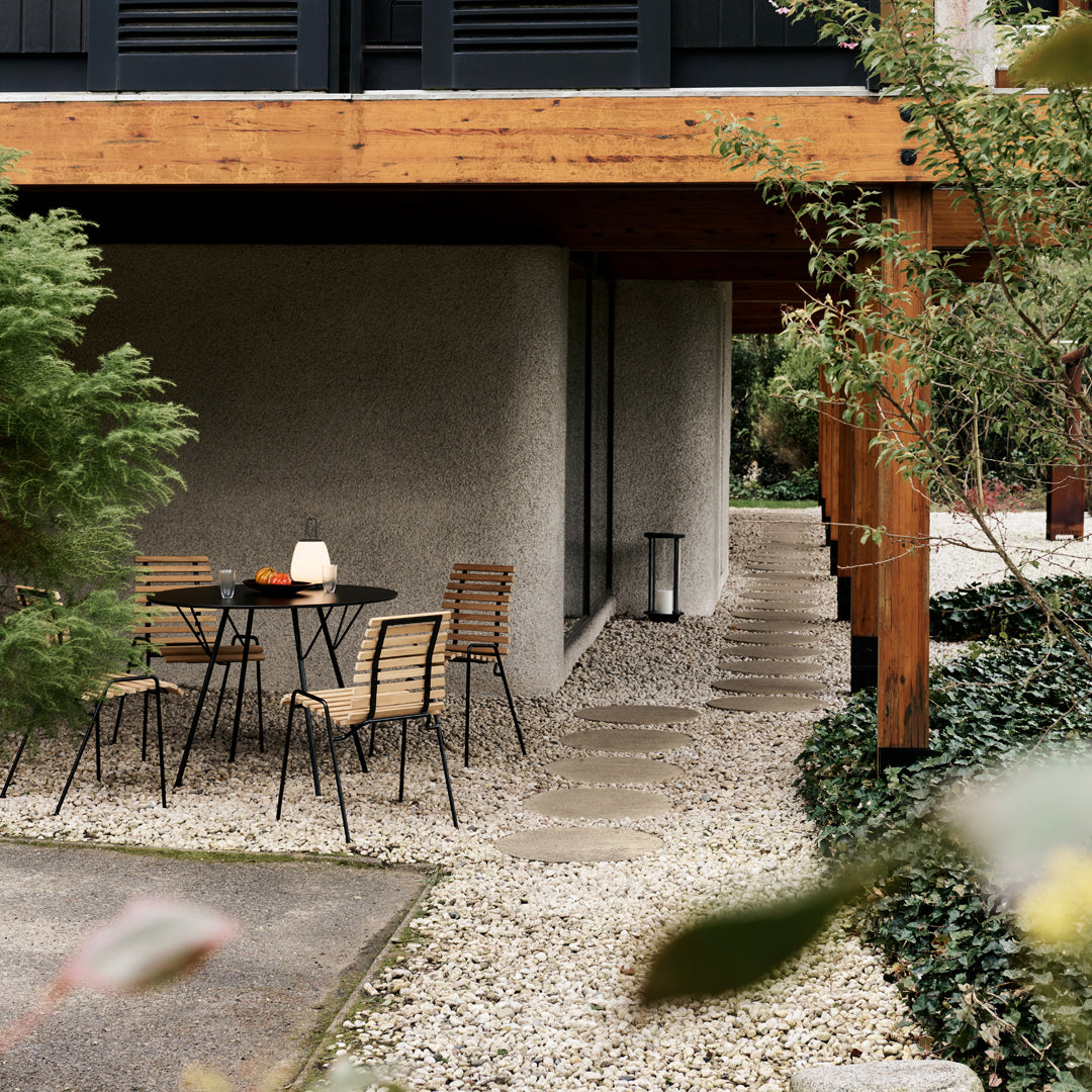 "Outdoor space with wooden accents, black chairs, and a gravel pathway surrounded by greenery."