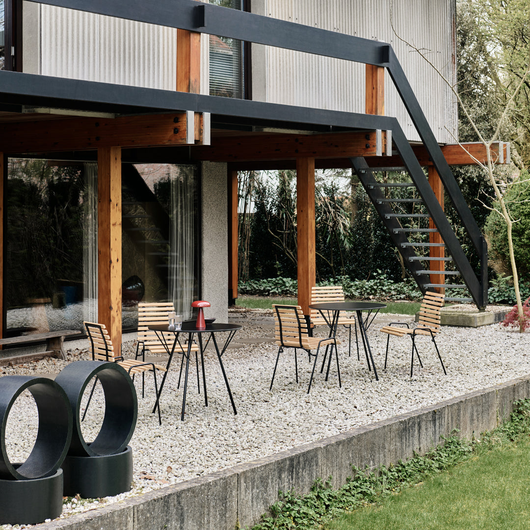 "Outdoor patio set featuring black metal chairs and table, natural wood accents, and a gravel surface with green grass."