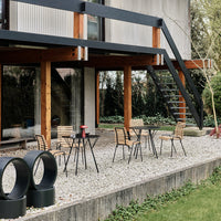 "Outdoor patio set featuring black metal chairs and table, natural wood accents, and a gravel surface with green grass."