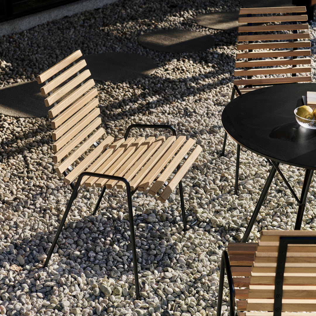 Slatted wooden chair with a natural finish and black metal frame, placed on a gravel surface. Ideal for outdoor settings.
