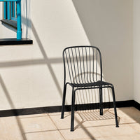 Black wire chair with sleek lines and a minimalist design, set against a light-colored wall.