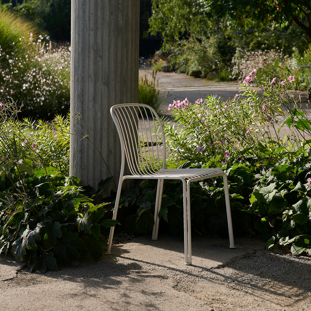 Minimalist white chair with vertical line pattern, set against lush greenery and soft floral accents.
