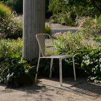 Minimalist white chair with vertical line pattern, set against lush greenery and soft floral accents.